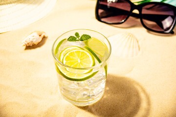 Summer fresh cocktail lemonade water with mint and lime citrus fruit on beach with white sand. Summer sea ocean vacation and travel concept