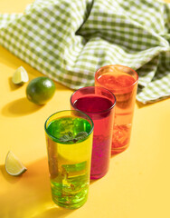 Summer fresh cocktail lemonade water with mint and lime citrus fruit in colorful glasses on yellow background