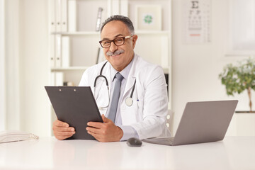 Mature doctor sitting in an office in front of a laptop computer