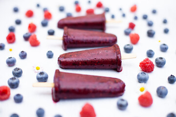 Four frozen ice cream popsicles made with raspberries and blueberries. Vertical or horizontal use. Summertime wallpaper. Selective focus.