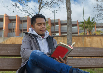 Fototapeta premium close up shot of a hispanic young man reading a book sitting on a park bench