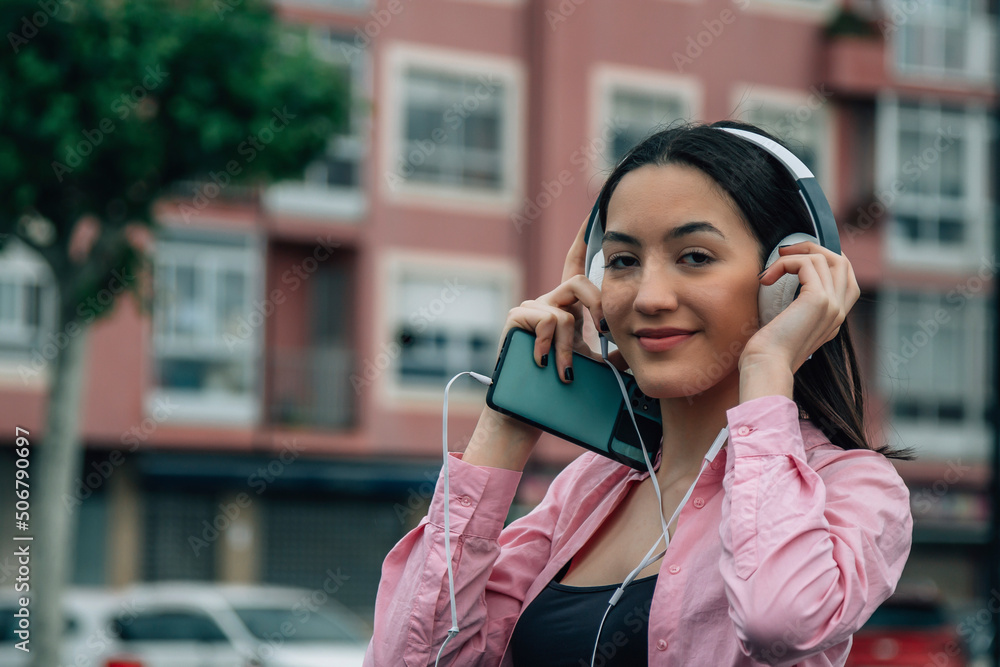 Wall mural young woman with headphones and mobile phone in the city