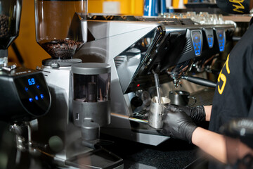 Close-up of Barista steaming milk for a hot cappuccino with a machine in a coffee shop. Process to...