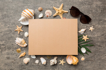 Summer time concept with blank greeting card and blank craft paper on colored background. Seashells from ocean shore in the shape of frame separated with space for text top view