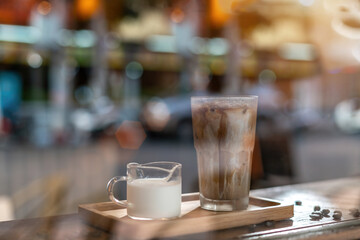 A tall glass of iced latte coffee with milk cream on a wooden counter bar over a cafe glass window reflex at a Cafe coffee shop. Cold brew refreshment summer drink with copy space Selective focus