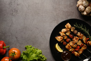 Grilled chicken meat skewers with fresh vegetables on dark stone background. Copy space for your text
