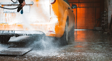 Washing a yellow car at a contactless self-service car wash. Washing a sedan car with foam and...