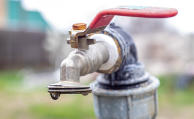 Water faucet on the background of nature. Opening or closing a faucet to save water indicates a water shortage problem. Rustic fountain with daylight. Selective focus with blurred background.