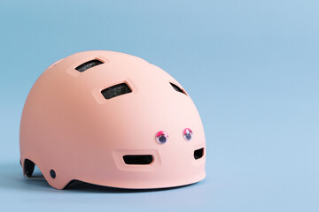 Pink helmet with funny doll eyes on blue background. Childs outdoors activity safety protection 