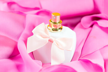 Women's white perfume bottle with pink bow on pink fabric