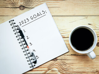 Open notebook with text “2023 Goals” and a cup  of coffee on wooden background.