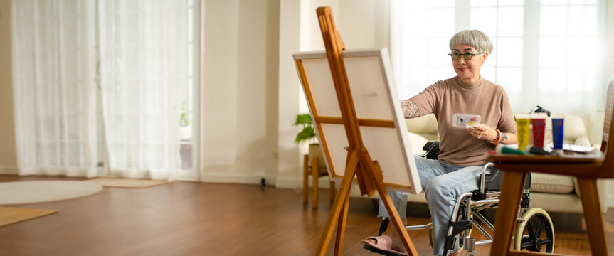 panoramic of disabled artist senior female drawing sitting on wheel chair at home.small business,entrepreneurship and Home hobby after retirement.Disabled Elderly female in wheelchair at art studio