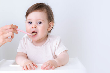Baby girl eating blend mashed food sitting, on high chair, mother feeding child, hand with spoon...