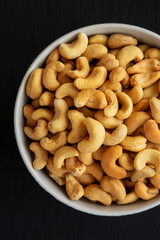 Homemade Roasted and Salted Cashews in a Bowl on a black background, top view. Flat lay, overhead, from above.