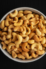 Homemade Roasted and Salted Cashews in a Bowl on a black surface, top view. Flat lay, overhead, from above.