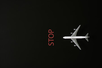 A toy white passenger airliner on a black background next to the inscription stop. The concept of a no-fly zone and non-flying weather. Selective focus. Copy space.