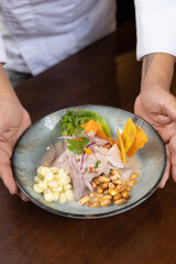 A vertical shoot of a hand of chef pushing a plate of ceviche