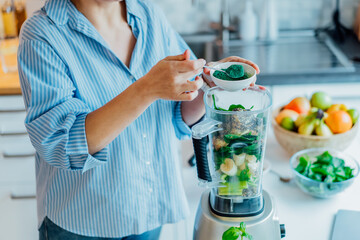Woman adding spirulina green powder during making green smoothie on the kitchen. Superfood...
