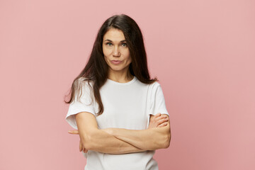 portrait of a beautiful, charismatic, attractive woman with dark hair color with arms crossed on her chest in a white cotton tank top on a pink background, with empty space