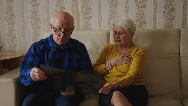 worried pensioner couple sitting on the sofa and looking at the x-ray results medium full shot indoor illness concept. High quality 4k footage