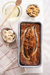 Chocolate banana bread with walnuts in a metallic baking mold and ingredients on a grey neutral background with creative lighting, top view