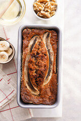 Chocolate banana bread with walnuts in a metallic baking mold and ingredients on a grey neutral background with creative lighting, top view