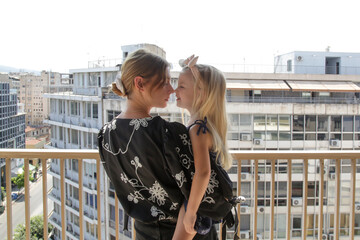 Mother and her little toddler standing on balcony with city buildings view	