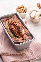 Chocolate banana bread with walnuts in a metallic baking mold and ingredients on a grey neutral background with creative lighting, top view