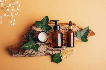 Bottle of cosmetic serum, facial cleanser and cream in a jar on tree bark with green leaves. Spa and wellness concept. Top view, flat lay
