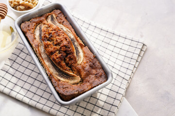 Chocolate banana bread with walnuts in a metallic baking mold on a grey neutral background, top view