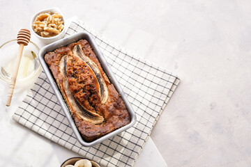 Chocolate banana bread with walnuts in a metallic baking mold on a grey neutral background, top view