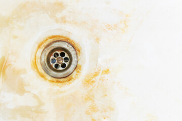An old rusty bathtub surface with a metal drain hole. Dirty cracked unclean bath or sink with red...