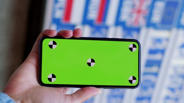 Money, exchange, market board. Woman using a smartphone green screen outside on money currency screen background. Close-up of female hand holding in vertical position green chromakey smartphone