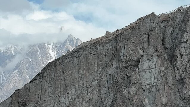 Aerial Dolly Left Across Mountain Wall To Reveal Passu Cones In the Karakoram Range Hiding In Clouds