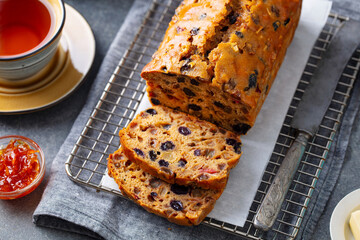Fruit cake Bara Brith on cooling rack. Welsh traditional dessert with cup of tea. Grey background....