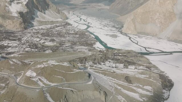 Aerial View Of Snow Covered Passu Village Beside Frozen Hunza River. Dolly Forward, Tilt Up View