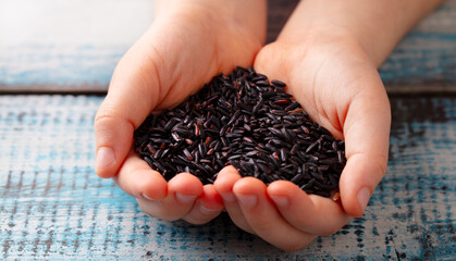 Black wild rice in kids hands. Wooden background. Close up.