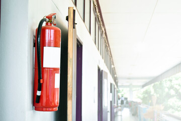 A red fire extinguisher is installed on a white cement wall in the front porch of the building to be used to extinguish a fire in the event of a building fire. - obrazy, fototapety, plakaty