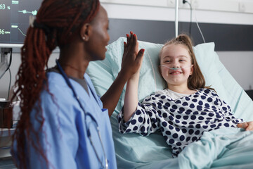 Pediatric hospital nurse highfive sick child while in patient treatment ward room. Blessed cheerful...