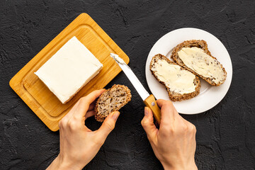 Hands spreading butter with knife on toast bread. Top view - obrazy, fototapety, plakaty