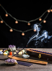 Burning incense stick and smoke, wooden base and wooden storage box for sticks on dark black background with semi precious stones crystals. Spirituality concept.
