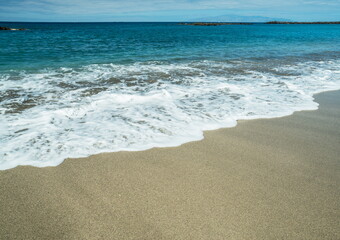 Ocean foam covering beautiful long sandy beach.