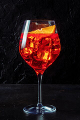 Aperol cocktail with an orange slice, a side view on a dark background, Italian summer cold drink