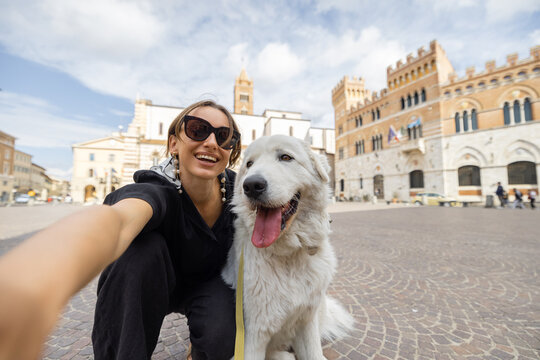 Woman takes selfie photo with dog traveling in Grosseto town the center of Maremma region in Italy. Maremmano abruzzese sheepdog that comes from this area of Italy. Concept of italian dog breed
