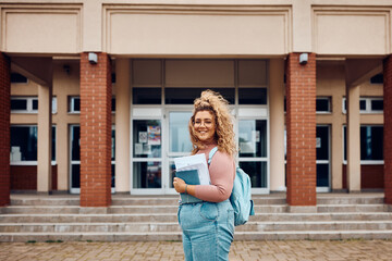 Portrait of happy female student in front of university looking at camera.