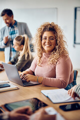 Happy female student using computer during class and looking at camera.