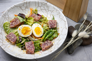 salad with tuna, lettuce, herbs, egg, on a gray table
