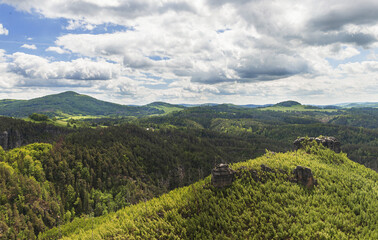Beautiful view of the landscape of Bohemian Switzerland. The photo shows rocks between trees and clouds in an otherwise blue sky. The photo is taken from the top of Maria Rock.