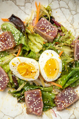 salad with tuna, lettuce, herbs, egg, on a gray table
