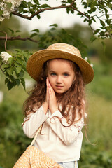 Beautiful girl in a straw hat against the backdrop of flowering gardens
